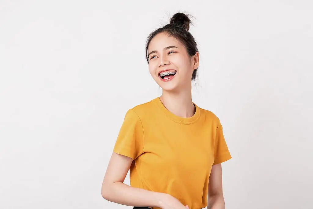 Young woman with braces wearing a yellow t-shirt smiles and looks to the side against a plain white background in Georgetown, TX.