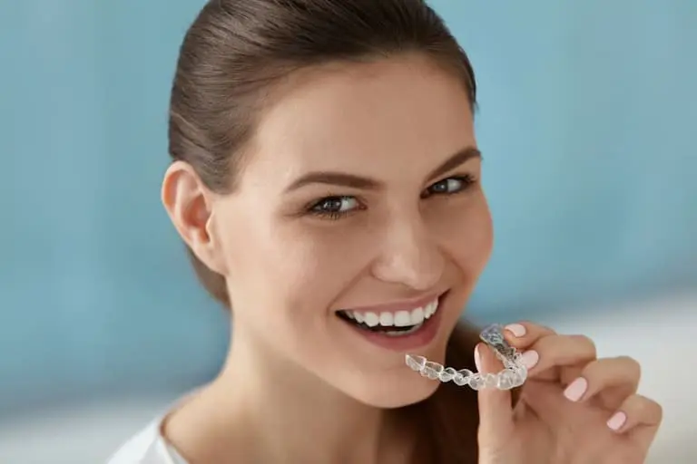 A woman smiles while holding a Invisalign Clear Aligners in Georgetown, TX