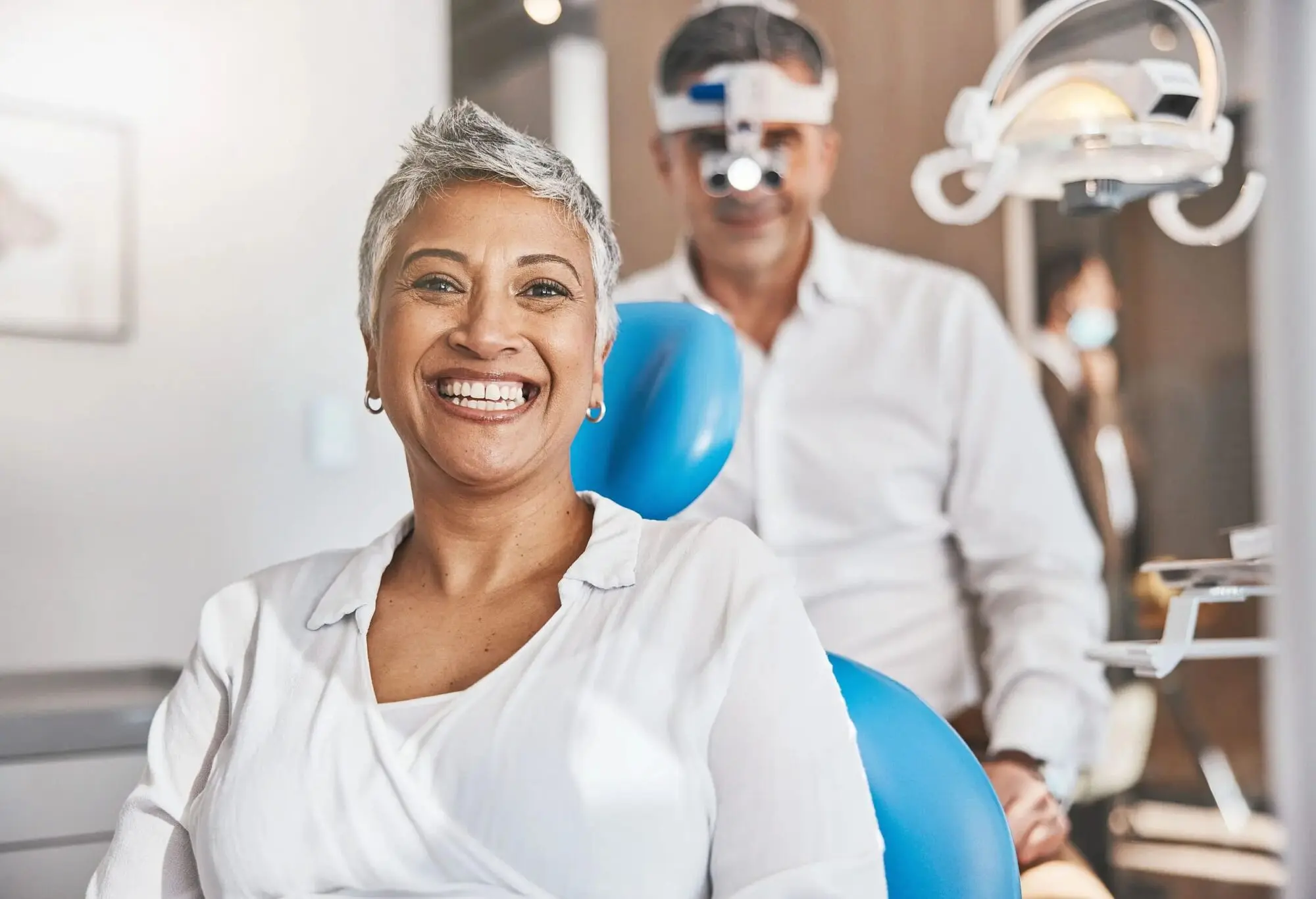Smiling woman sits in a dental chair with Orthodontics Expert wearing magnifying glasses standing behind her at Farr Orthodontics in Georgetown, TX.