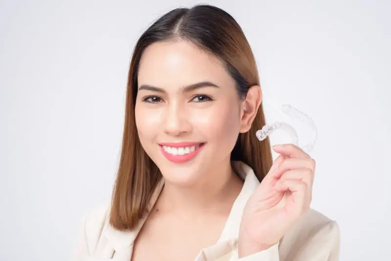 A woman smiles while holding a Invisalign Clear Aligners in Georgetown, TX
