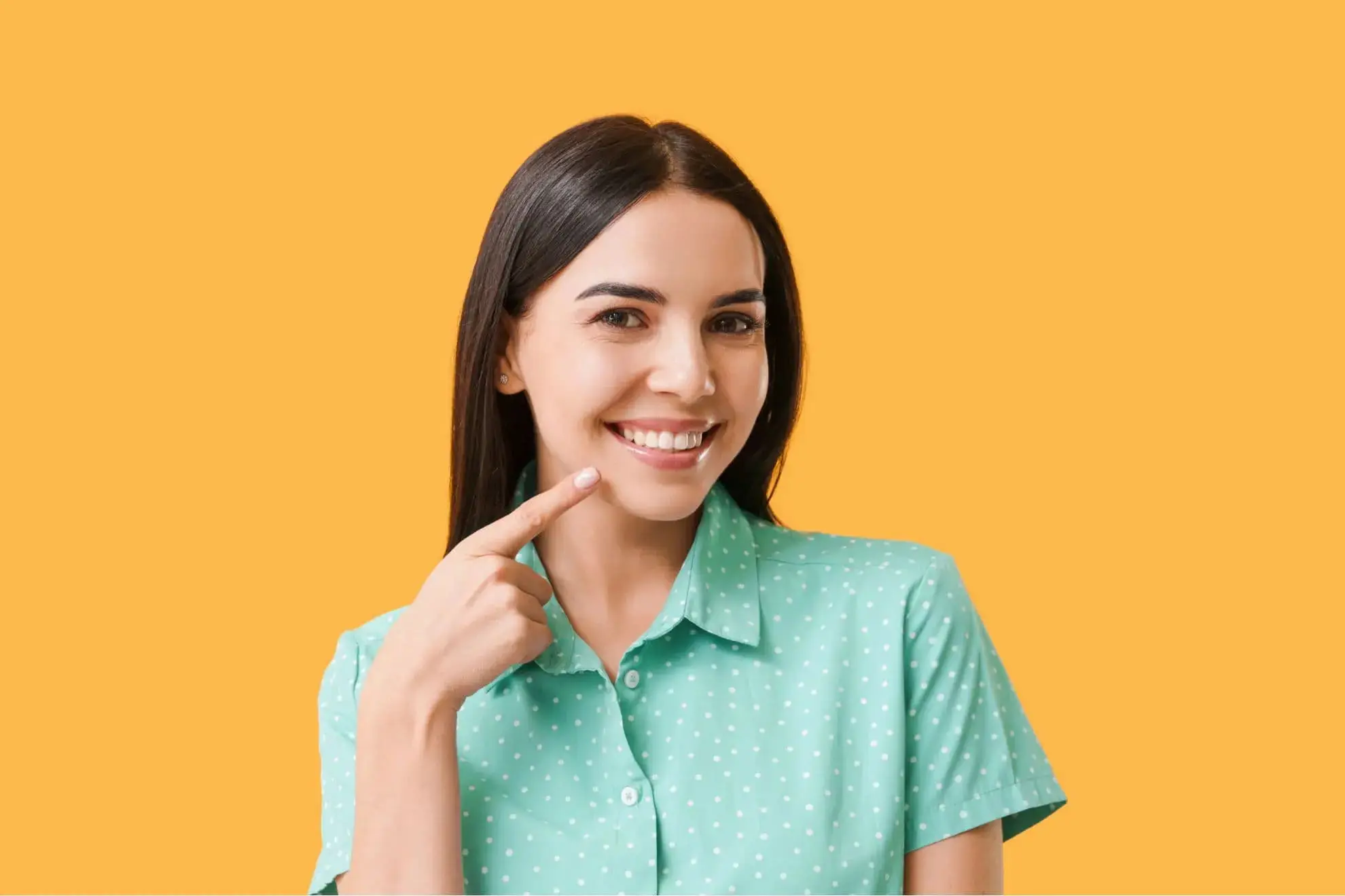 Smiling woman in a green polka dot shirt points to her result by orthodontic appliances at Farr Orthodontics Georgetown in Georgetown, TX.
