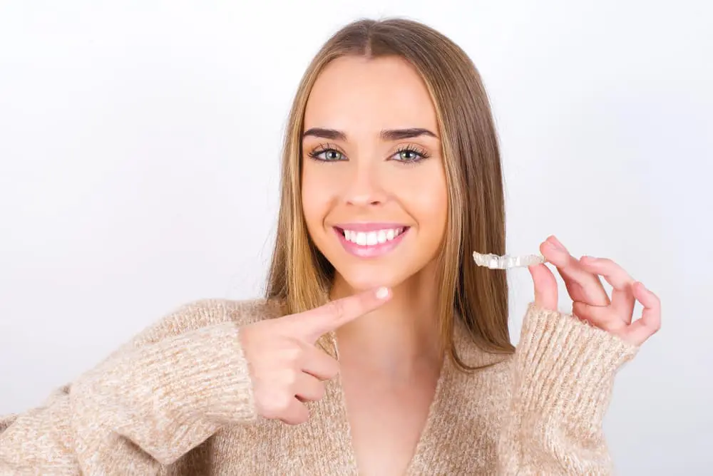 Smiling, a long-haired woman points to her clear aligner Invisalign at Farr Orthodontics in Georgetown, TX.