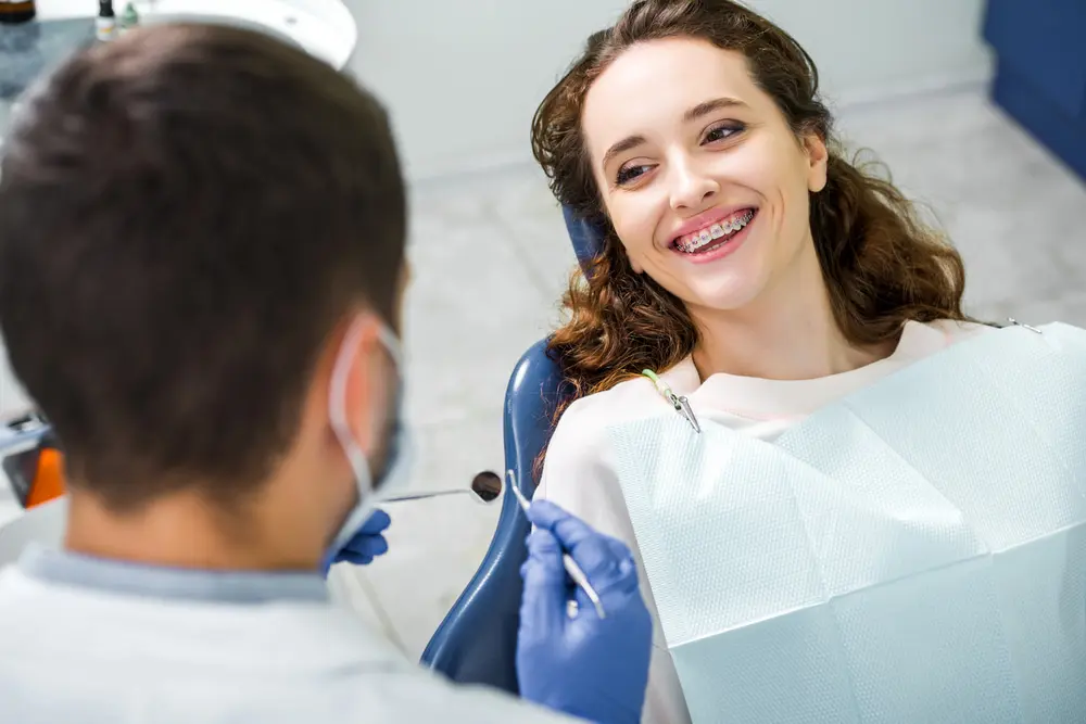 At Farr Orthodontics in Georgetown, TX, a young woman with braces smiles at a masked dentist during a free orthodontic consultation for braces.