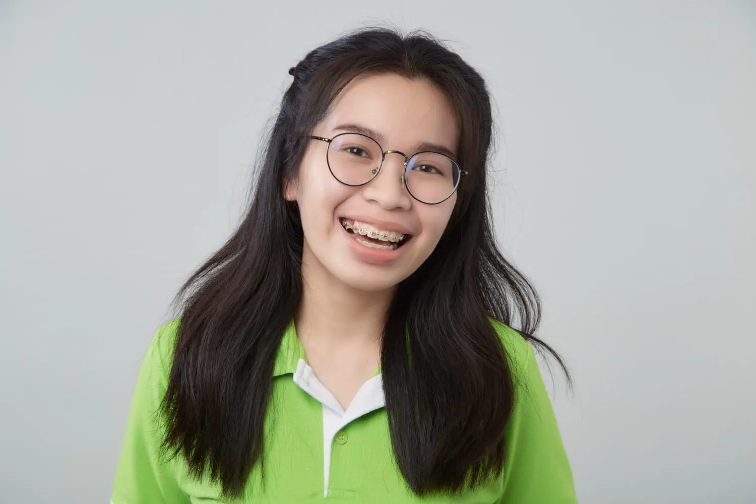 Farr Orthodontics A young person in a green shirt with glasses and braces smiles confidently, showing their Farr Orthodontics results in Georgetown, TX, and reflecting great Braces Cost value.