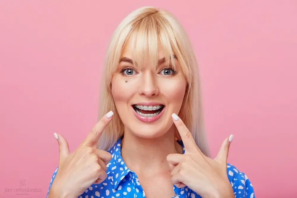 cheerful happy young woman blonde hair gesturing thumb while pointing clear braces - How Long Do Braces Take in Georgetown, TX 