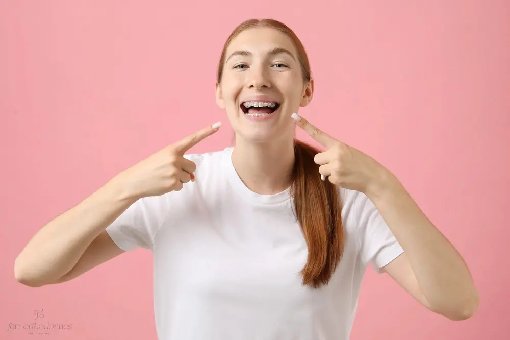 girl pointing her metal braces pink background - How Long Do Braces Take in Georgetown, TX 