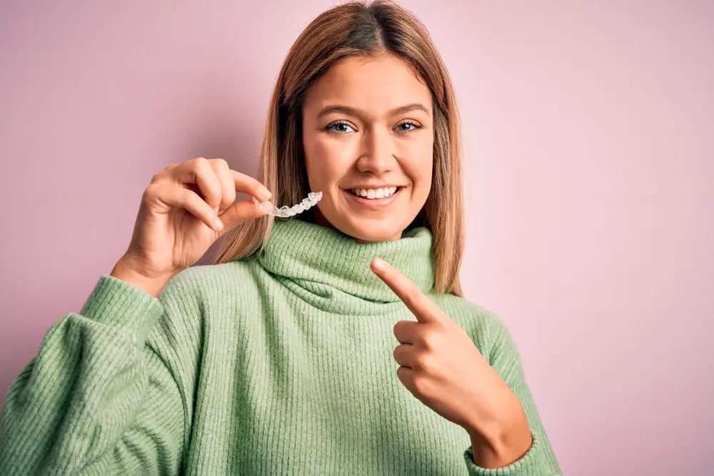 young beautiful woman holding invisalign clear aligners standing isolated pink background - How Does Invisalign Work in Georgetown, TX 